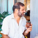 A man smiling while enjoying a traditional yerba mate drink outdoors.